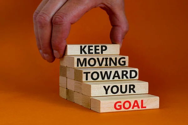 Keep moving toward your goal symbol. Wooden blocks with words Keep moving toward your goal. Beautiful orange background, copy space. Businessman hand. Business, your goal concept.