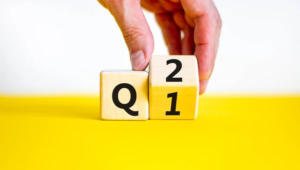 Birinci çeyrekten ikinci çeyreğe kadar. İşadamı tahta küpü döndürür ve 'Q1' i 'Q2' ye çevirir. Güzel sarı masa, beyaz arka plan. İş dünyası, mutlu 2. çeyrek Q2 konsepti, kopyalama alanı.