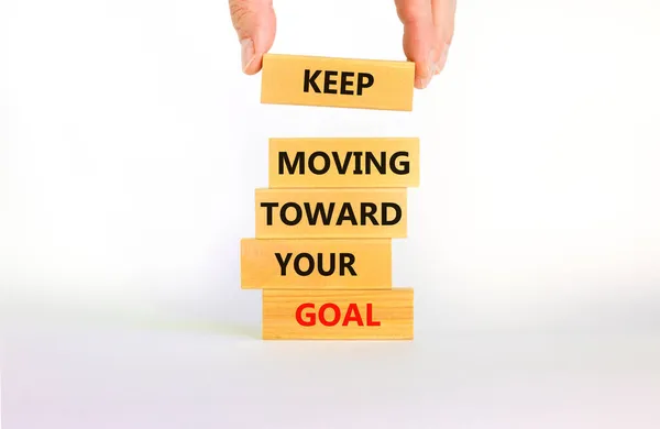 Keep moving toward your goal symbol. Wooden blocks with words Keep moving toward your goal. Beautiful white background, copy space. Businessman hand. Business, your goal concept.