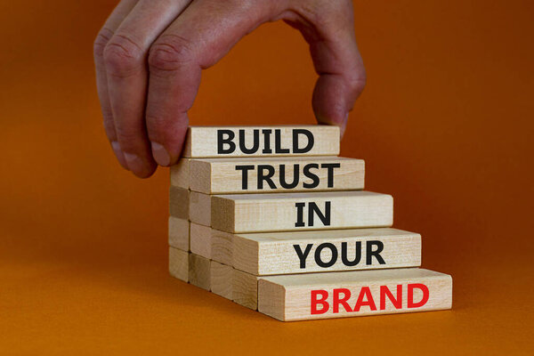 Success business process symbol. Wood blocks stacking as step stair on orange background, copy space. Businessman hand. Words 'build trust in your brand'. Business and trust brand concept.