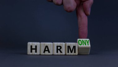 Zarardan armoniye. İş adamı ahşap küpü döndürür ve kelime zararını ahenge çevirir. Güzel gri masa, gri arka plan. İş ve zarar ya da uyum kavramı. Boşluğu kopyala.