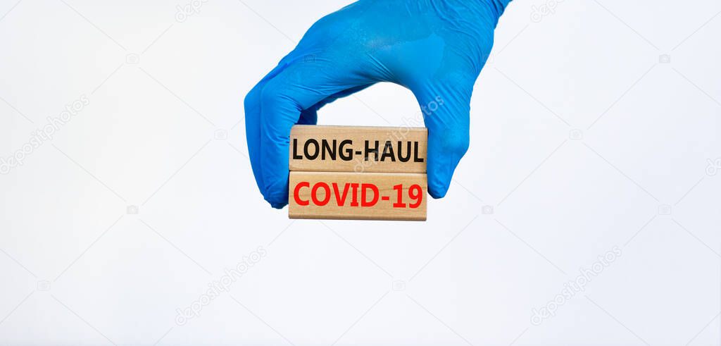 COVID-19 long-haul covid symptoms symbol. Wooden blocks words Long-haul covid-19. Doctor hand, blue glove, beautiful blue background, copy space. Medical, COVID-19 long-haul covid-19 symptoms concept.