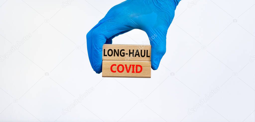COVID-19 long-haul covid symptoms symbol. Wooden blocks with words long-haul covid. Doctor hand, blue glove, beautiful blue background, copy space. Medical, COVID-19 long-haul covid symptoms concept.