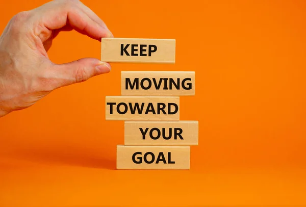Keep moving toward your goal symbol. Wooden blocks with words Keep moving toward your goal. Businessman hand. Beautiful orange background, copy space. Business, your goal concept.