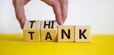 Beyin takımı sembolü. İşadamı ahşap küpleri dönüştürür ve 'tank' kelimesini 'düşünmek' ya da tam tersi olarak değiştirir. Güzel sarı masa, beyaz arka plan, kopyalama alanı. İş, beyin takımı konsepti.