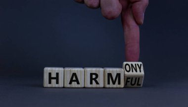 Zararlıdan uyumluya. İş adamı ahşap küpü döndürür ve sözcüğü uyuma zararlı hale getirir. Güzel gri masa, gri arka plan. İş ve zararlı ya da uyum kavramı. Boşluğu kopyala.