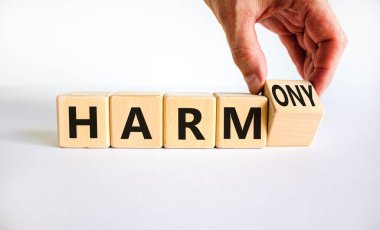 Zarardan armoniye. İş adamı ahşap küpü döndürür ve kelime zararını ahenge çevirir. Güzel beyaz masa, beyaz arka plan. İş ve zarar ya da uyum kavramı. Boşluğu kopyala.