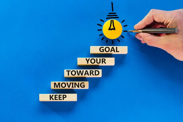 Keep moving toward your goal symbol. Wooden blocks with words Keep moving toward your goal. Light bulb icon. Businessman hand, pen. Blue background, copy space. Business, your goal concept.
