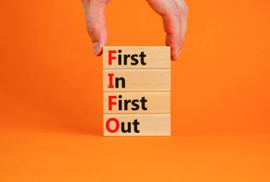 FIFO ilk çıkış sembolü. Tahta bloklarda ilk önce FIFO 'nun girdiği kavramsal kelimeler. Güzel turuncu masa, turuncu arka plan. İşadamı eli. İş FIFO 'su ilk giriş ve çıkış konsepti. Boşluğu kopyala.