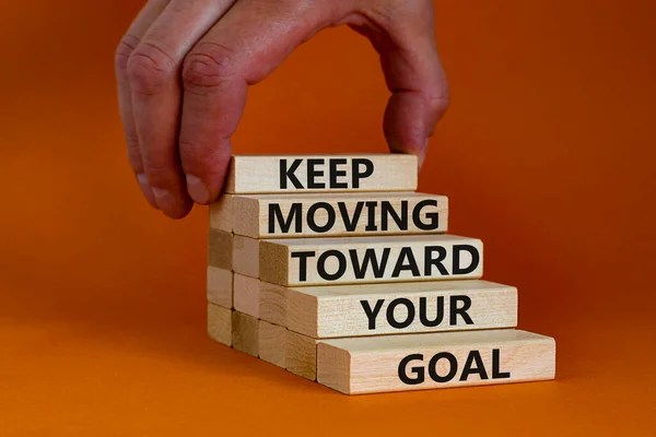 Keep moving toward your goal symbol. Wooden blocks with words Keep moving toward your goal. Beautiful orange background, copy space. Businessman hand. Business, your goal concept.