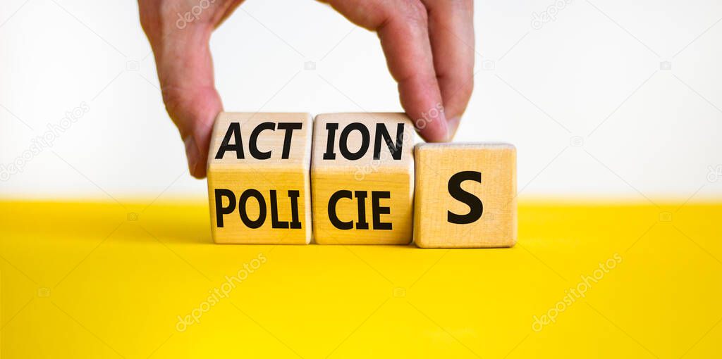 Actions and policies symbol. Businessman turns wooden cubes and changes the word policies to action. Beautiful yellow table, white background, copy space. Business actions and policies concept.