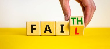 Faith instead fail symbol. Businessman turns a wooden cube and changes the word fail to faith. Beautiful yellow table, white background. Business and faith instead fail concept. Copy space.