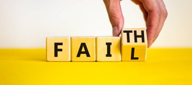 Faith instead fail symbol. Businessman turns a wooden cube and changes the word fail to faith. Beautiful yellow table, white background. Business and faith instead fail concept. Copy space.