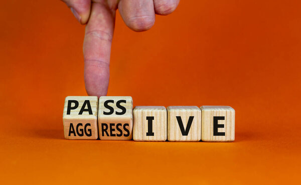 Пассивный или агрессивный символ. Бизнесмен превращает деревянные кубики и превращает слово пассивное в агрессивное. Красивый оранжевый фон, копия пространства. Бизнес, психологическая пассивная агрессия.