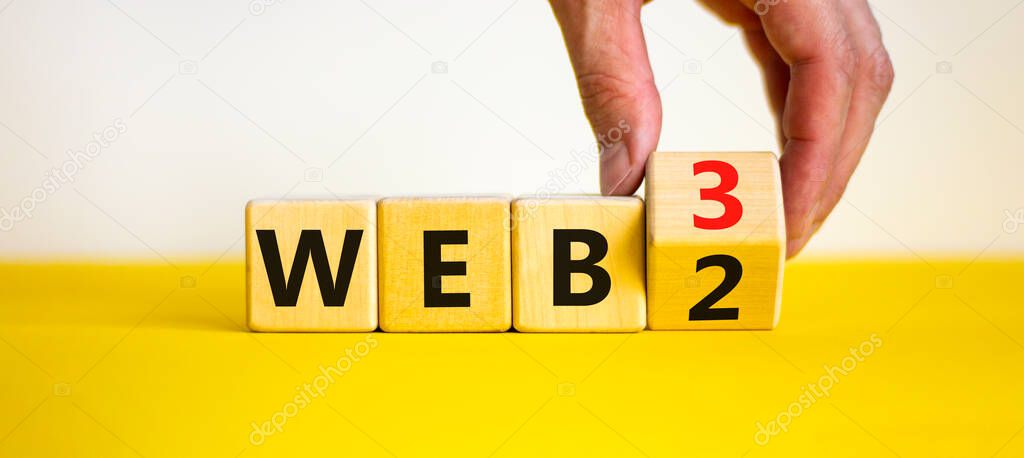WEB 2 or 3 symbol. Businessman turns a wooden cube and changes words WEB 2 to WEB 3. Beautiful yellow table, white background, copy space. Business, technology and WEB 2 or 3 concept.