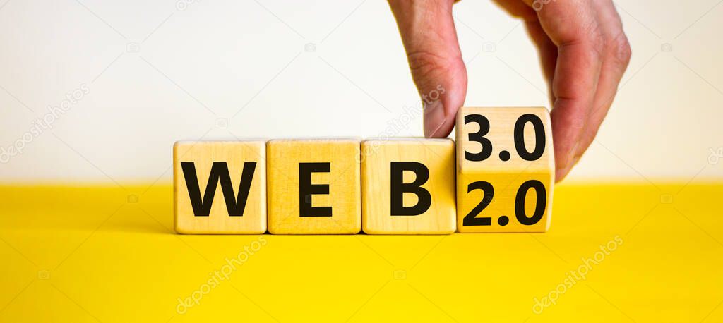 WEB 2.0 or 3.0 symbol. Businessman turns a wooden cube and changes words WEB 2.0 to WEB 3.0. Beautiful yellow table, white background, copy space. Business, technology and WEB 2.0 or 3.0 concept.