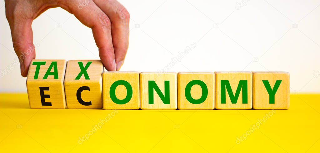 Taxonomy or economy symbol. Businessman turns cubes, changes the word economy to taxonomy. Beautiful yellow table, white background, copy space. Business, ecology and taxonomy or economy concept.
