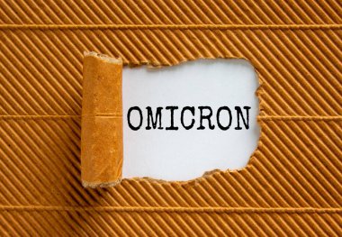 Covid-19 Corona ve Omicron sembolü. Omicron konsepti yırtık kahverengi kağıdın arkasında beliriyor. Güzel kahverengi ve beyaz arka plan. Tıbbi covid-19 Corona omicron konsepti. Boşluğu kopyala.