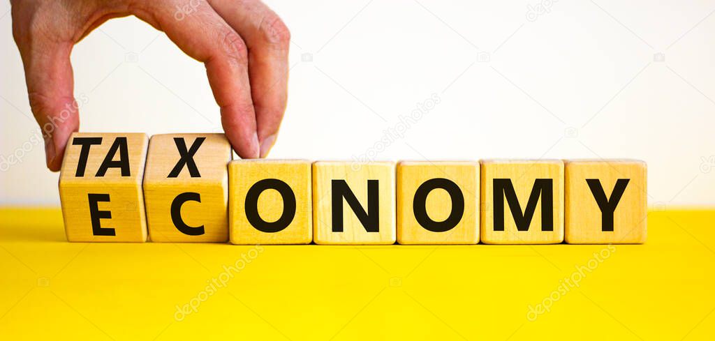 Taxonomy or economy symbol. Businessman turns cubes, changes the word economy to taxonomy. Beautiful yellow table, white background, copy space. Business, ecology and taxonomy or economy concept.