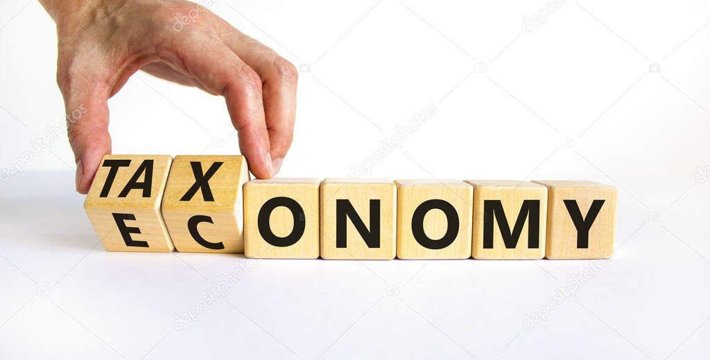 Taxonomy or economy symbol. Businessman turns cubes, changes the word economy to taxonomy. Beautiful white table, white background, copy space. Business, ecology and taxonomy or economy concept.