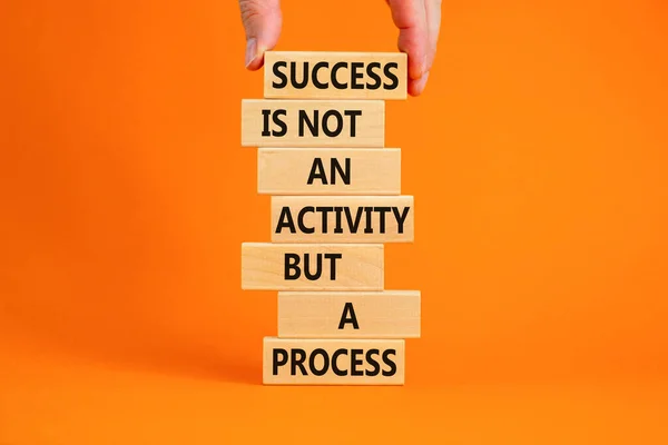 Success in process symbol. Wooden blocks with words Success is not an activity but a process. Beautiful orange background, copy space. Businessman hand. Business, success in process concept.