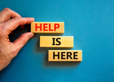 Yardım ve destek sembolü burada. Kavramsal kelimeler Yardım burada ahşap bloklarda güzel mavi masa arka planında. İşadamı eli. İş, destek, yardım kavramı burada. Boşluğu kopyala.