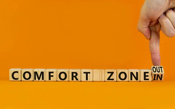 Out or in comfort zone symbol. Businessman turns wooden cubes and changes words Comfort zone in to Comfort zone out. Beautiful orange background, copy space. Business, psychology comfort concept.