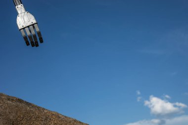 Mavi gökyüzündeki yapay zeka teknolojisi ve insanlar arasındaki bağlantının bir sembolü olarak erkek insan ve robotun elleri