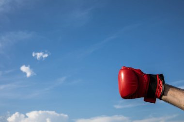 Elle boks eldiveninin dövüşmeye hazır görüntüsü. Mavi bulutlu arka plan üzerinde kırmızı boks eldiveni var. Kazanan, zafer, şampiyon, motivasyon konsepti.