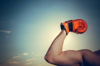 Mavi bulutlu arka plan üzerinde boşluk olan kırmızı boks eldiveni giyen bir eli kapat. Kazanan, zafer, şampiyon, motivasyon konsepti.