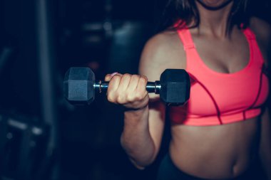 Spor salonundaki spor kadın halterlerle kaslarını şişiriyor. Genç sporcu seksi fitness kadın vücudu. Koyu arka planda duran halterler..