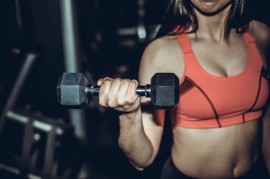 Spor salonundaki spor kadın halterlerle kaslarını şişiriyor. Genç sporcu seksi fitness kadın vücudu. Koyu arka planda duran halterler..