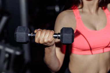 Spor salonundaki spor kadın halterlerle kaslarını şişiriyor. Genç sporcu seksi fitness kadın vücudu. Koyu arka planda duran halterler..