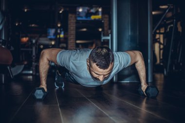 Adam ağır bir dambılla egzersiz yapıyor. Spor giysileri giyen ve tavan arasında egzersiz yaparken kalas pozisyonu alan kaslı, kaslı genç bir adam..