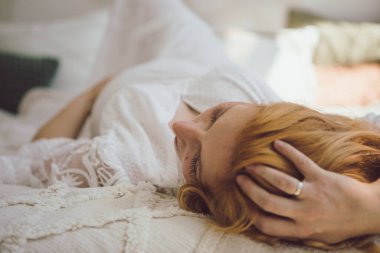 Avrupalı hamile kadın evdeki kanepede dinleniyor. Hamile kızıl saçlı kadın evde rahat bir yatakta uzanıyor..