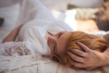 Avrupalı hamile kadın evdeki kanepede dinleniyor. Hamile kızıl saçlı kadın evde rahat bir yatakta uzanıyor..