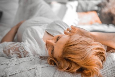 Avrupalı hamile kadın evdeki kanepede dinleniyor. Hamile kızıl saçlı kadın evde rahat bir yatakta uzanıyor..