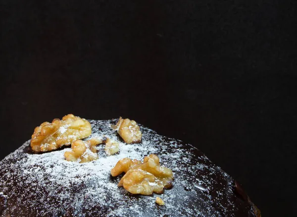 A panettone with nut topping on a black background