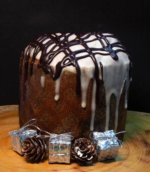 Ahşap bir masada panettone, siyah bir zemin, Noel süsleriyle çevrili.