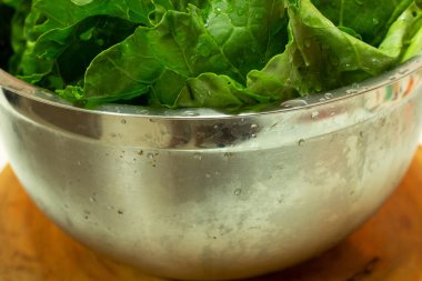 Ahşap arka planda paslanmaz çelikten bir kasenin içinde lahana yaprakları var.