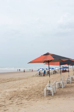 Güneşli bir günde plaj sandalyeleri, güneş şemsiyeleri ve plajdaki insanlarla dolu güzel bir manzara..