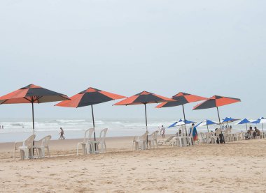 Güneşli bir günde plaj sandalyeleri, güneş şemsiyeleri ve plajdaki insanlarla dolu güzel bir manzara..