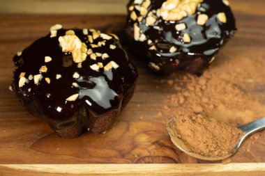 Tahta bir masada iki çikolatalı kek, bir kaşık dolusu çikolata tozunun yanında.