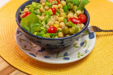 Masadaki mavi kasede yapraklı, zeytinli ve domatesli nohut kaşığı