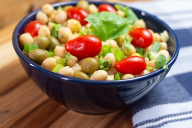 Masadaki mavi kasede yapraklı, zeytinli ve domatesli nohutlar.