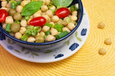 Masadaki mavi kasede yapraklı, zeytinli ve domatesli nohut kaşığı