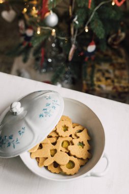 Bokeh arka planlı, rahat bir evde, beyaz masadaki porselen kasede cam lekeli Noel kurabiyeleri. Eğlenceli ve yaratıcı aşçılık projesi. Ev destekli yaşam tarzı. 