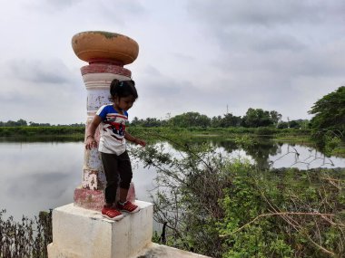 Channapatna, Karnataka, Hindistan-Aug 15, 2021: Göletin yanındaki Taş Sütun 'un önünde duran Hintli kız çocuğuna yakın çekim