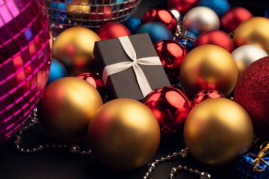Noel topları arasında farklı renk ve boyutlarda bir hediye kutusu.