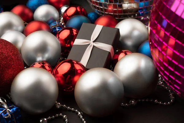 Noel topları arasında farklı renk ve boyutlarda bir hediye kutusu.